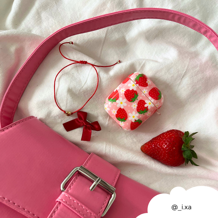 Pink purse, red string bracelet, ribbon, and Coconut Lane Airpods case with berry print on white fabric.