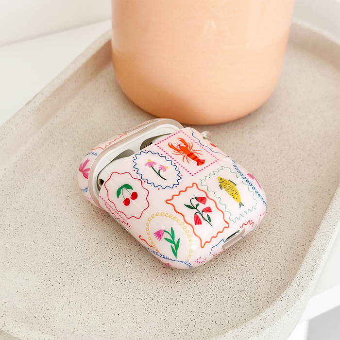 Coconut Lane Airpods Case with bright fruit and animal print, shown on a speckled tray next to a peach-colored pot.