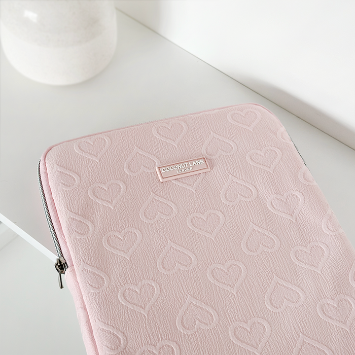 Baby pink iPad sleeve with embossed heart pattern, displayed on a white surface.