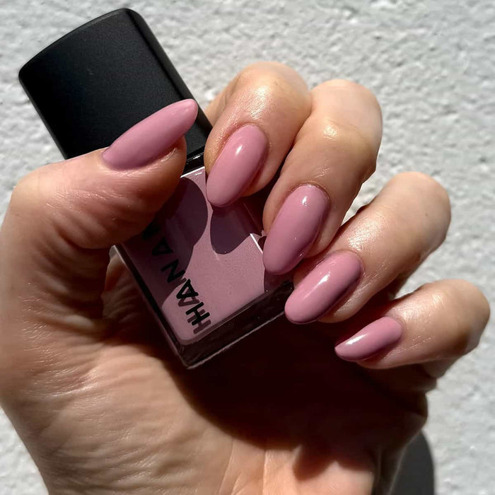 Hand holding a pink nail polish bottle with matching nails against a neutral background.