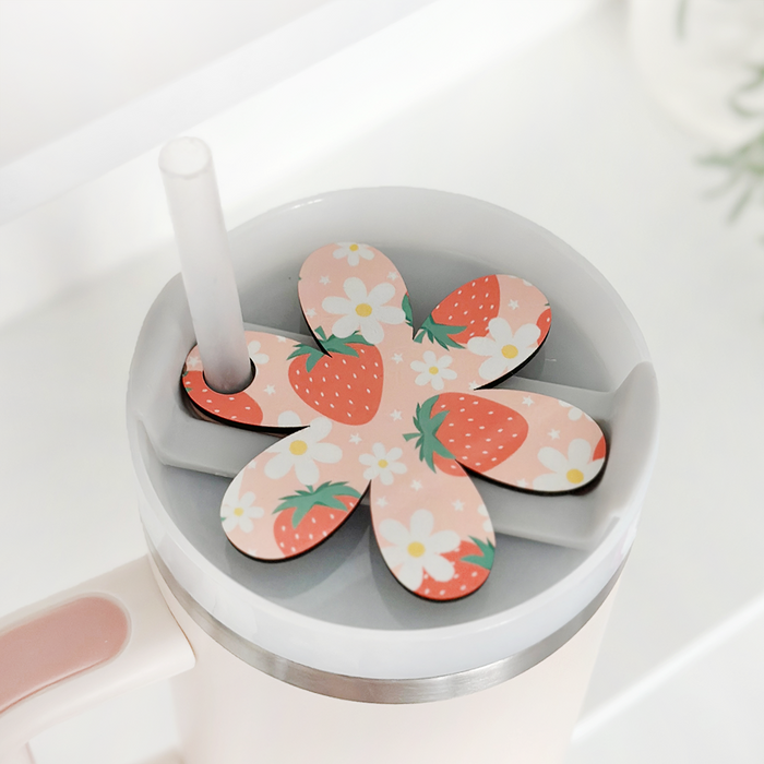 Pink tumbler with straw, topped with a Coconut Lane flower-shaped topper decorated with strawberries and floral designs.