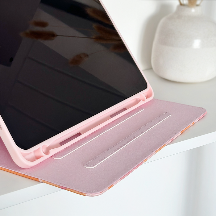 Pink and orange floral Coconut Lane iPad case holding a tablet on a white surface next to a white ceramic vase.