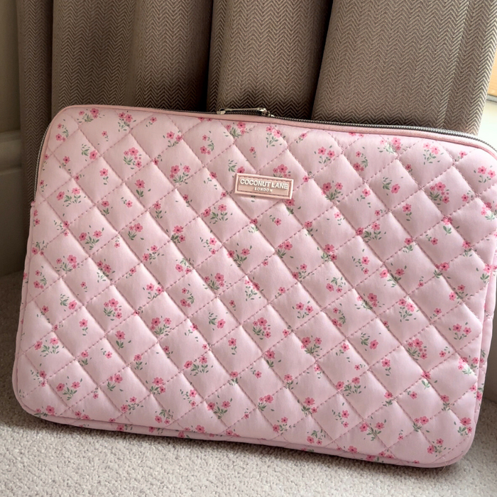 Coconut Lane pink quilted laptop sleeve with ditsy floral pattern, shown on a carpeted floor by beige curtains.