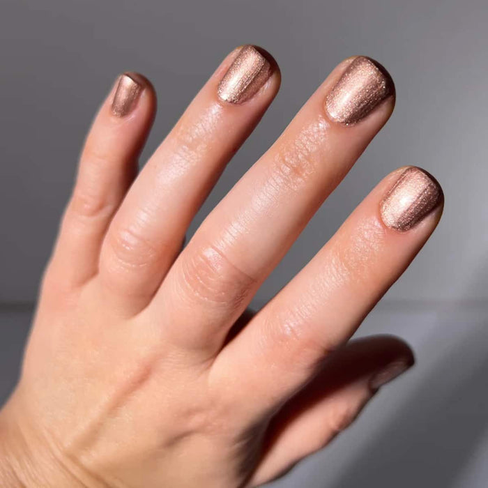 Hand with rose gold nail polish on a neutral background.