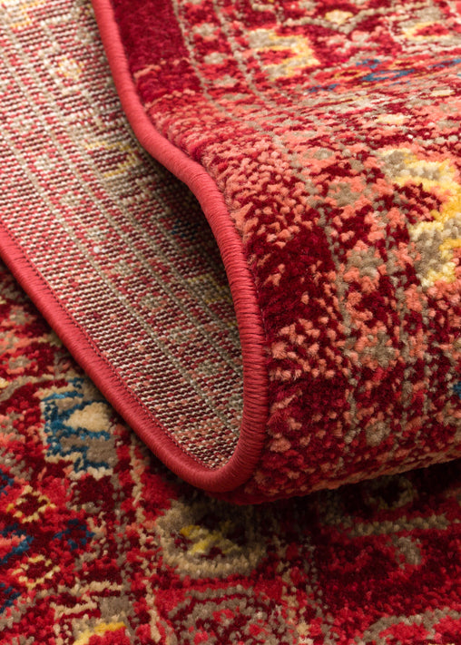 Red traditional rug with a distressed floral medallion pattern and blue and gold accents, shown folded to reveal backing.