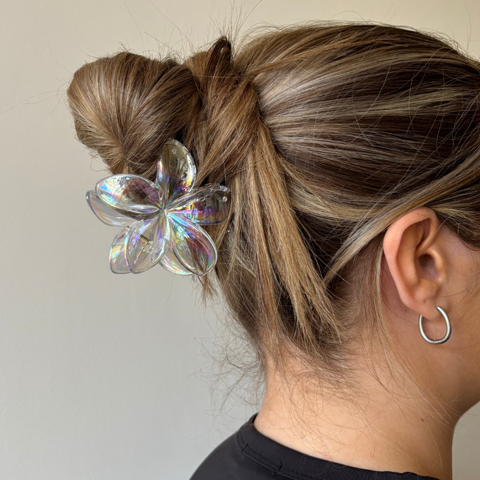 Hair in a bun secured with a holographic clear Tropical Flower claw clip; silver hoop earring visible.