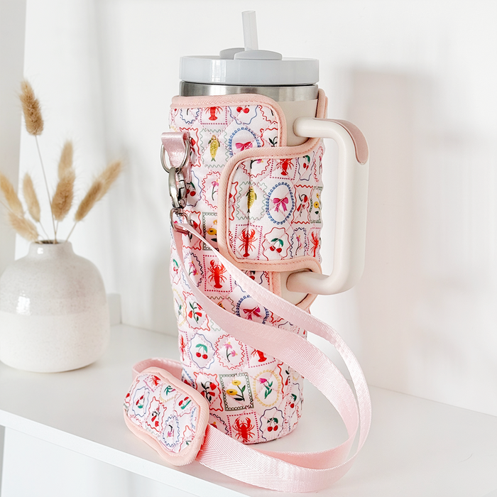 Quilted beige Coconut Lane tumbler carry case with Stanley Quencher 40oz on a white shelf next to dried grasses.