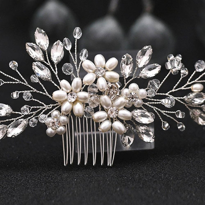 A silver hair comb adorned with pearl and crystal flowers and leaves, featuring intricate wirework and sparkling details, shimmers elegantly against a dark background.