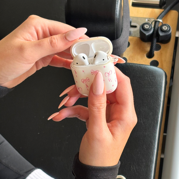 Hand holding open a Coconut Lane AirPods case with a dainty bows pattern. Manicured nails visible.