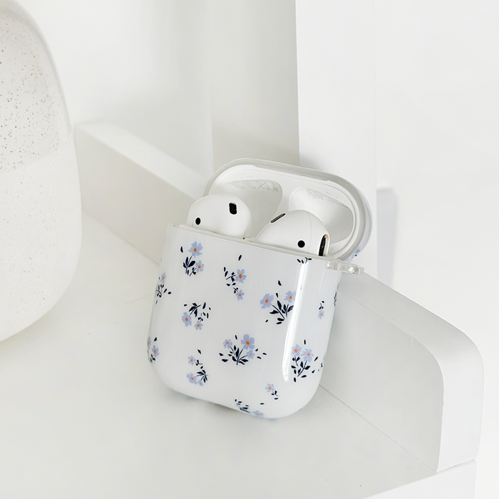 White wireless earbuds with a blue floral Coconut Lane AirPods case, set on a white surface.