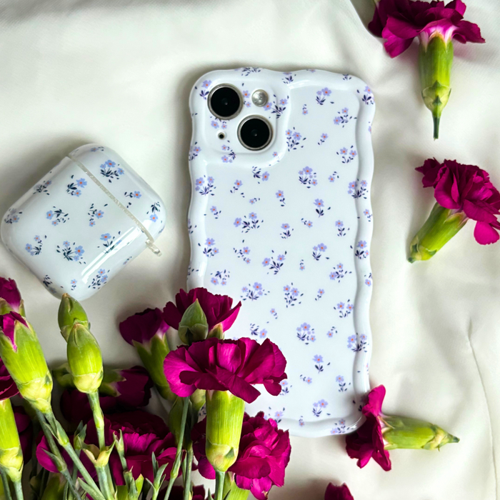 Ditsy floral periwinkle AirPods case and white phone case on white fabric with magenta flowers.