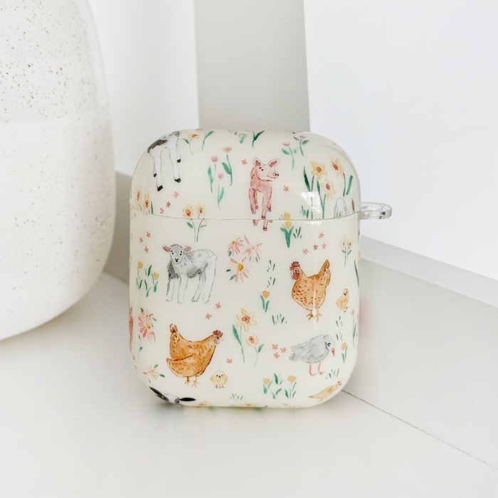 Coconut Lane AirPods case with a white finish, decorated with illustrated chickens, sheep, pigs, and colorful flowers.
