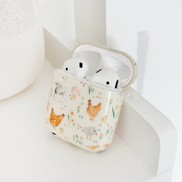 White AirPods in a Coconut Lane case featuring colorful farmyard animal illustrations, placed on a white surface.