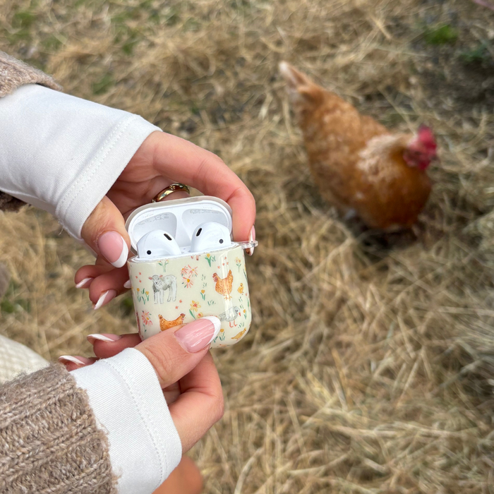 Hands hold a Farmyard Friends AirPods case by Coconut Lane; a brown chicken stands in the background.