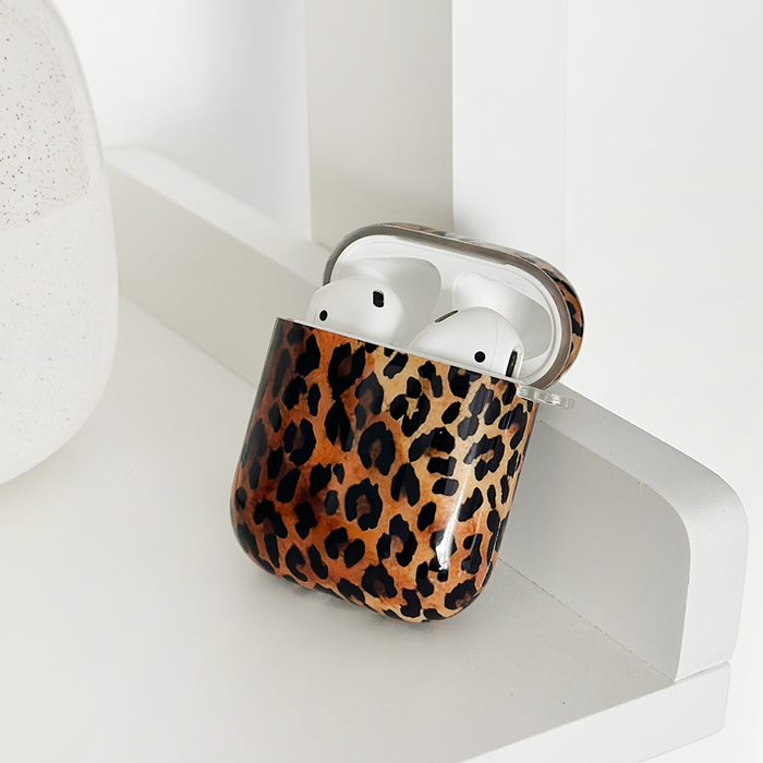 Leopard print Coconut Lane AirPods case with AirPods on a white shelf next to a white ceramic ornament.