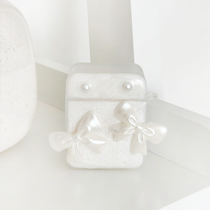 Coconut Lane Airpods case with pearl studs and shiny bows, displayed on a white shelf.