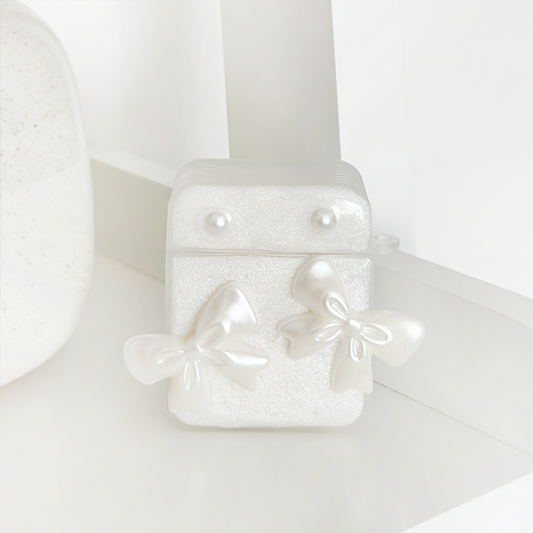 Coconut Lane Airpods case with pearl studs and shiny bows, displayed on a white shelf.
