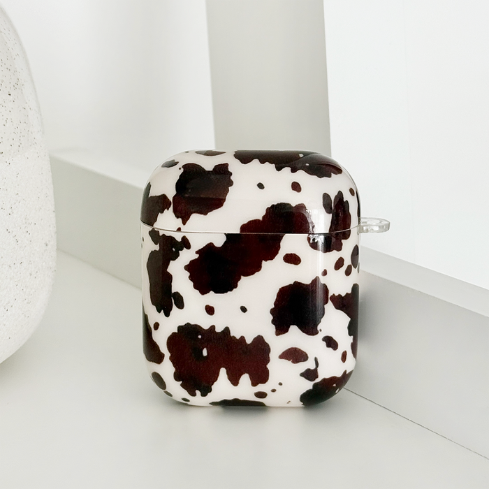 Black and white cow-print AirPods case on a white shelf next to a textured decor item.
