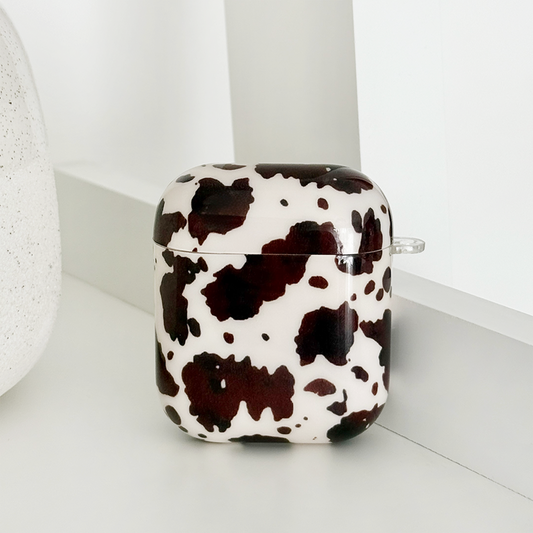 Black and white cow-print AirPods case on a white shelf next to a textured decor item.