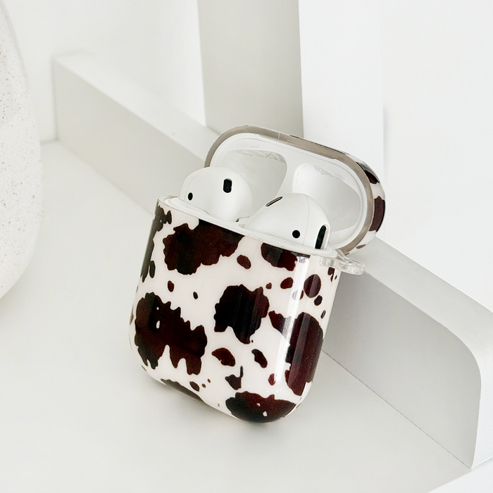 White wireless earbuds in a pink and brown Rodeo Cowgirl AirPods case on a clean white surface.