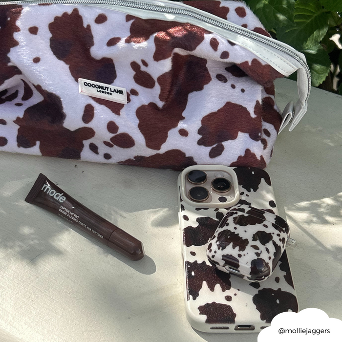 Cow print pouch, matching phone case, brown Coconut Lane AirPods case, and a brown lip crayon on a white surface.