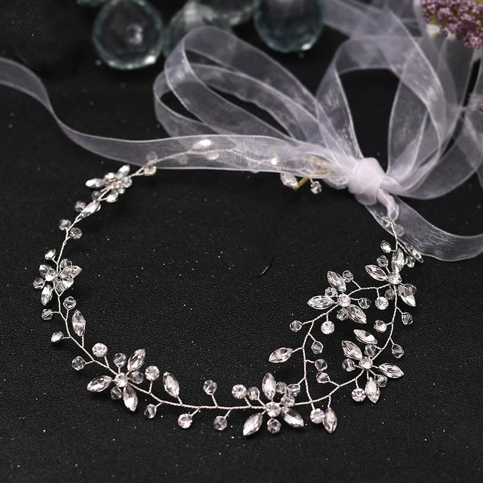 A delicate silver floral headpiece adorned with clear crystal beads and sheer white ribbon forms a stunning circular design for special occasions.