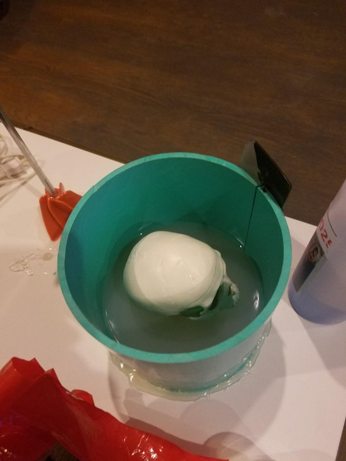 Beginning process of silicone mold making with small skull sitting in a green pot.