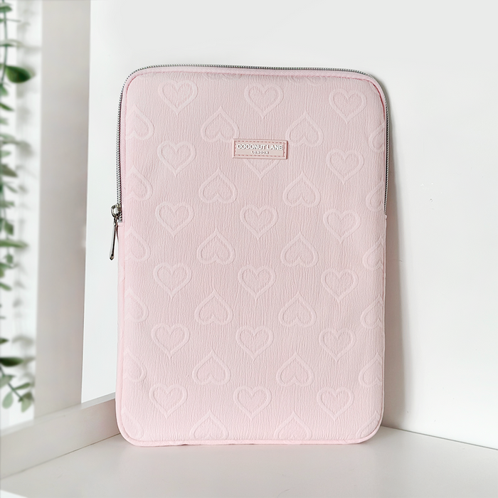Baby pink iPad sleeve with embossed heart pattern and zipper, standing upright on a white background.