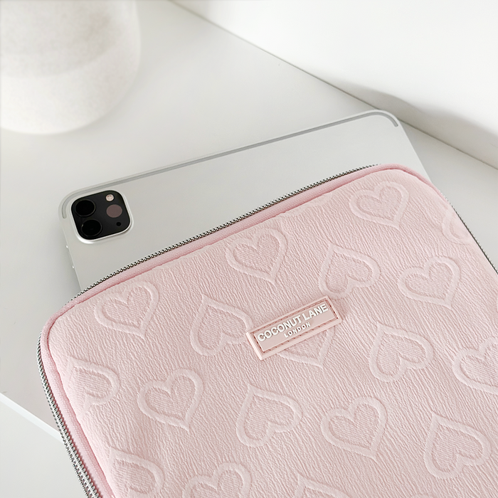 Baby pink iPad sleeve with white hearts by Coconut Lane on a white surface.