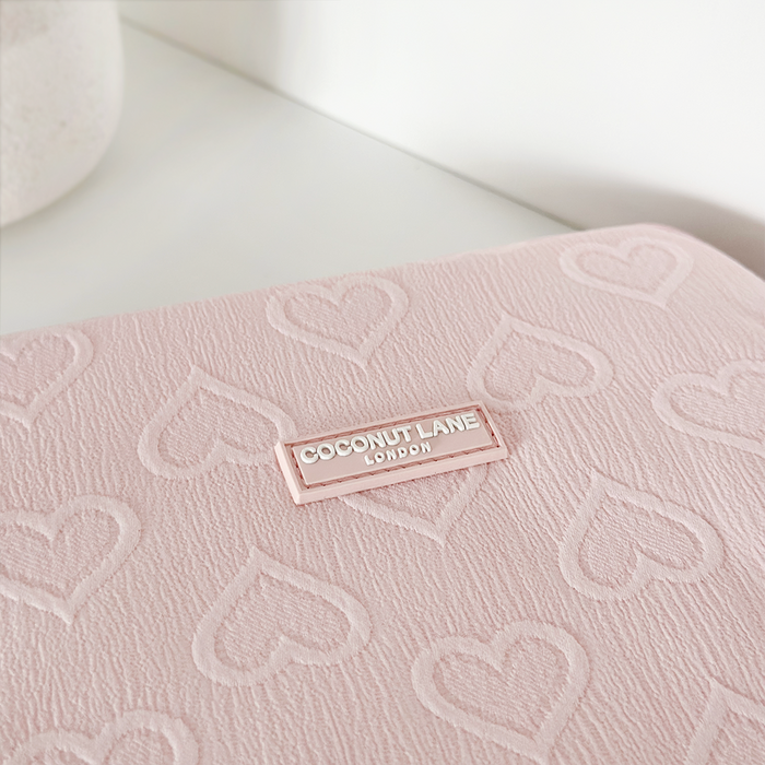 Baby pink iPad sleeve with embossed hearts and a Coconut Lane label, shown on a white surface.
