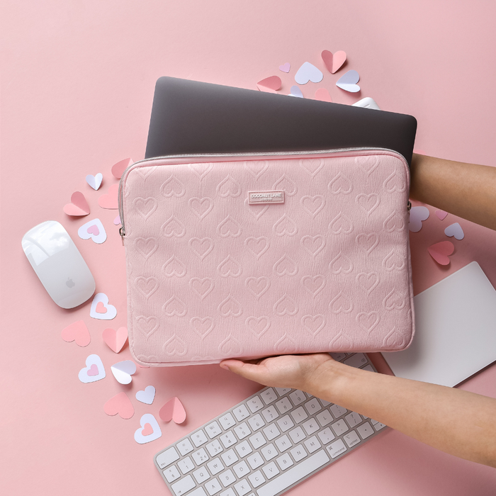Laptop being placed in a pink heart-patterned Coconut Lane sleeve on a pink desk with matching keyboard and mouse.