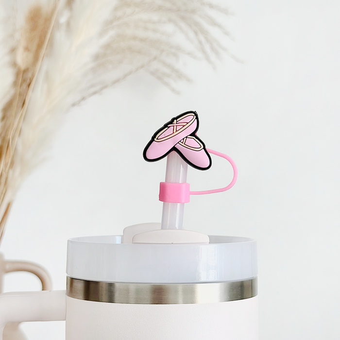 Pink ballet slippers straw cover on a white tumbler, with pampas grass softly blurred in the background.