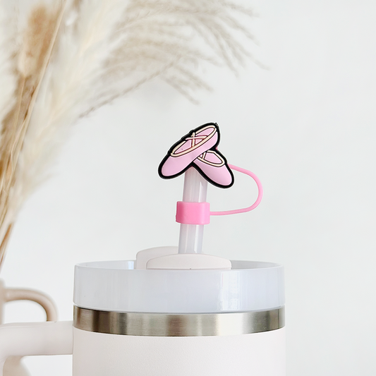 Pink ballet slippers straw cover on a white tumbler, with pampas grass softly blurred in the background.