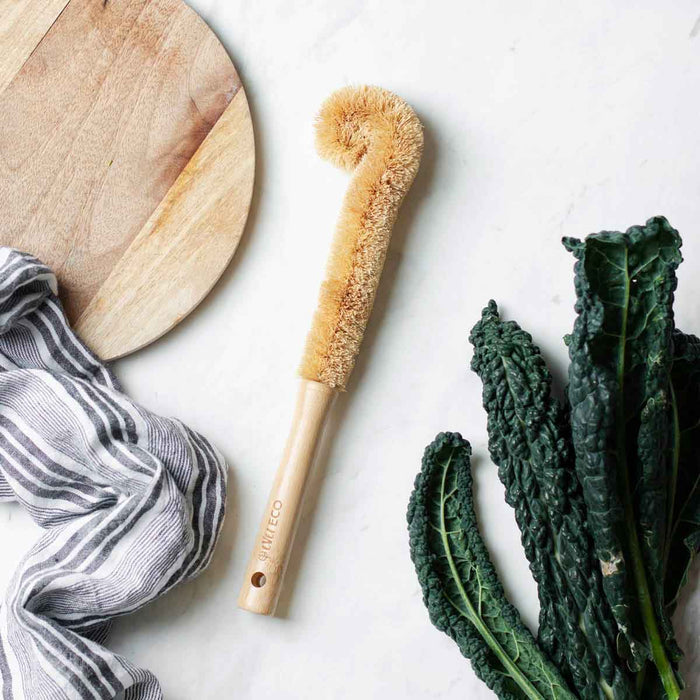 Bottle brush styled on a kitchen bench with cutting board, kale & a striped linen towel.
