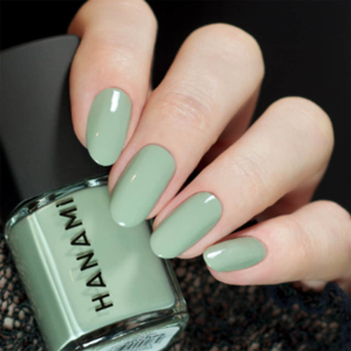 Hand with green nails holding a bottle of Hanami nail polish.