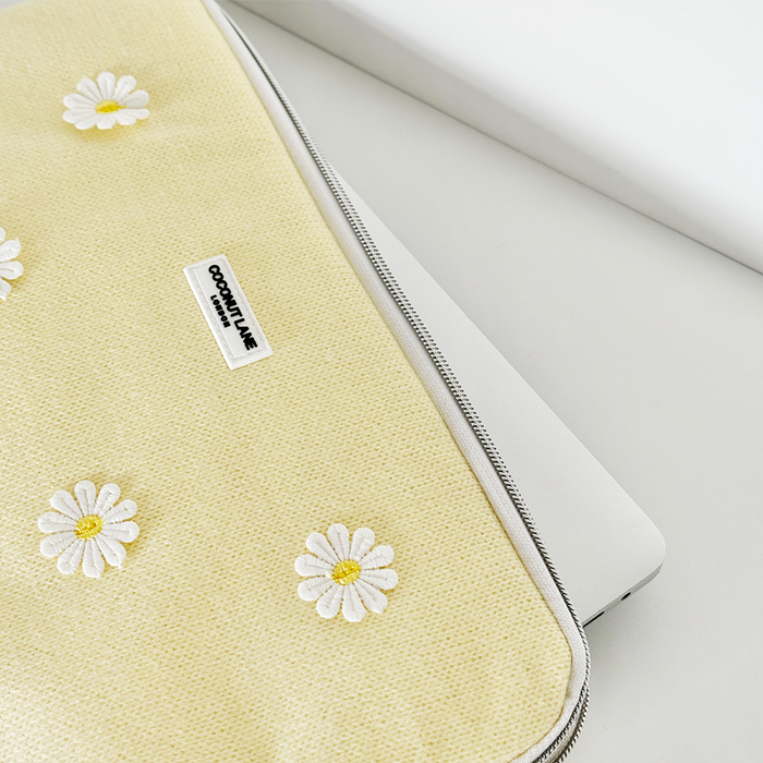 Buttercup Bloom laptop sleeve with white daisy pattern partially covering a silver laptop on a white surface.