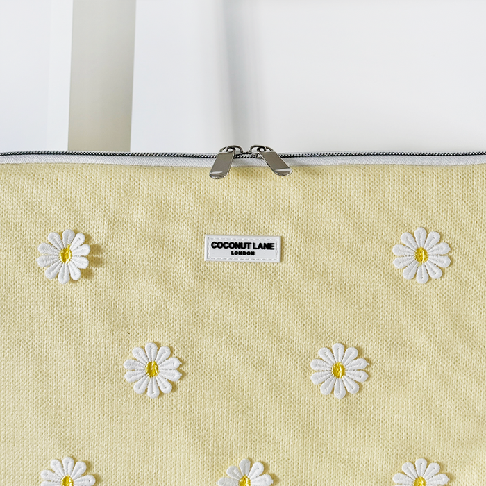 Yellow laptop sleeve with buttercup and white daisy print, Coconut Lane label, and silver zipper.
