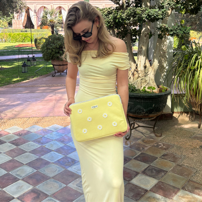 Woman in a pale yellow off-shoulder dress holds a floral Buttercup Bloom laptop sleeve on a sunny patio.