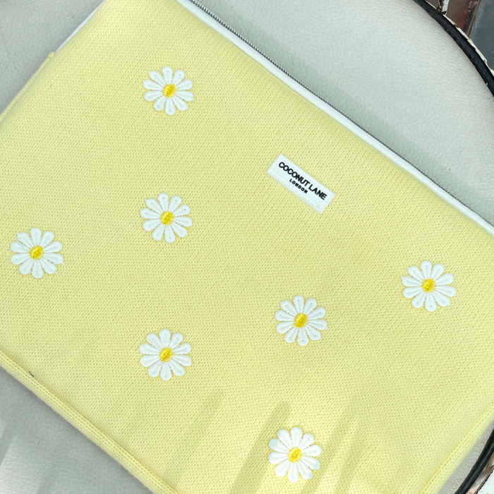 Yellow laptop sleeve with white embroidered daisies, Buttercup Bloom design by Coconut Lane, shown on a light surface.