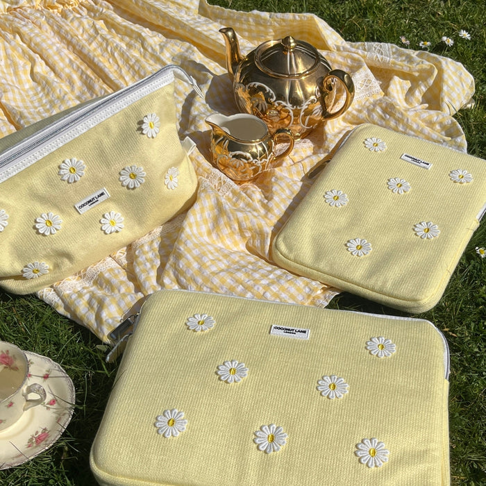 Yellow iPad sleeve with daisy embroidery on a picnic blanket, next to a gold tea set.