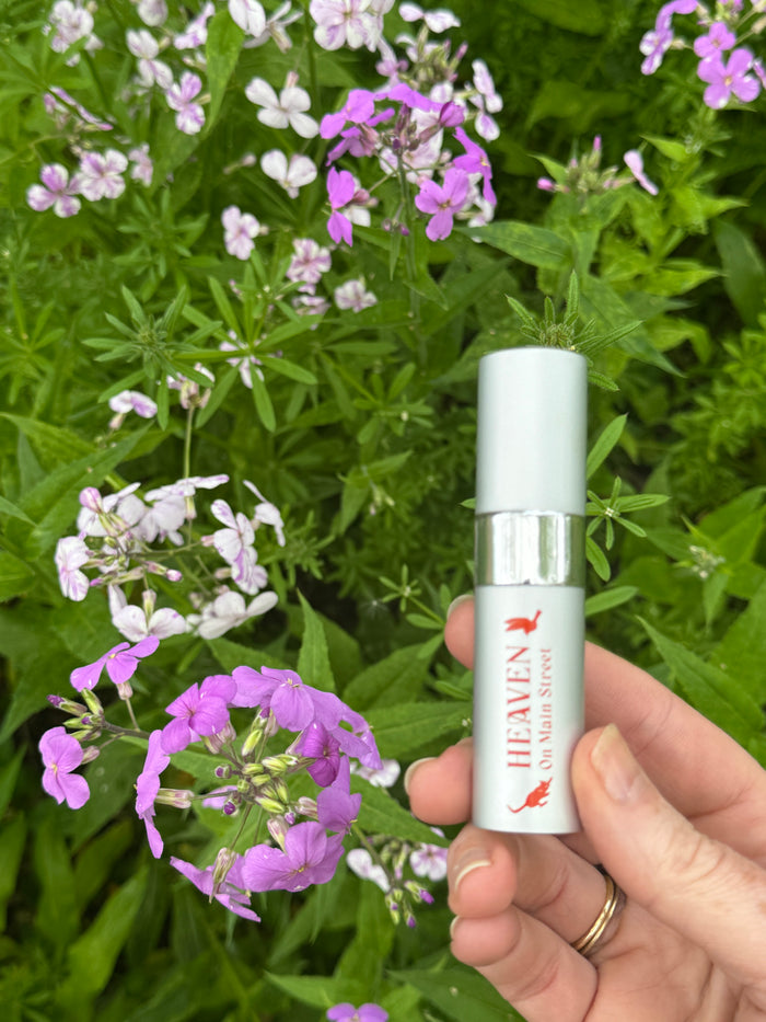 Hand holding a small bottle labeled 'Heaven' among flowers