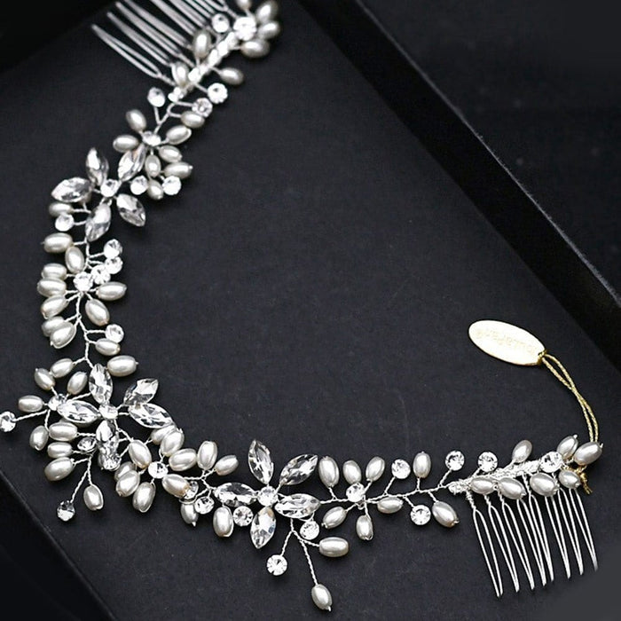 A delicate silver hair accessory with crystal and pearl-like beads in a leafy floral design, combs at both ends, on a black surface.
