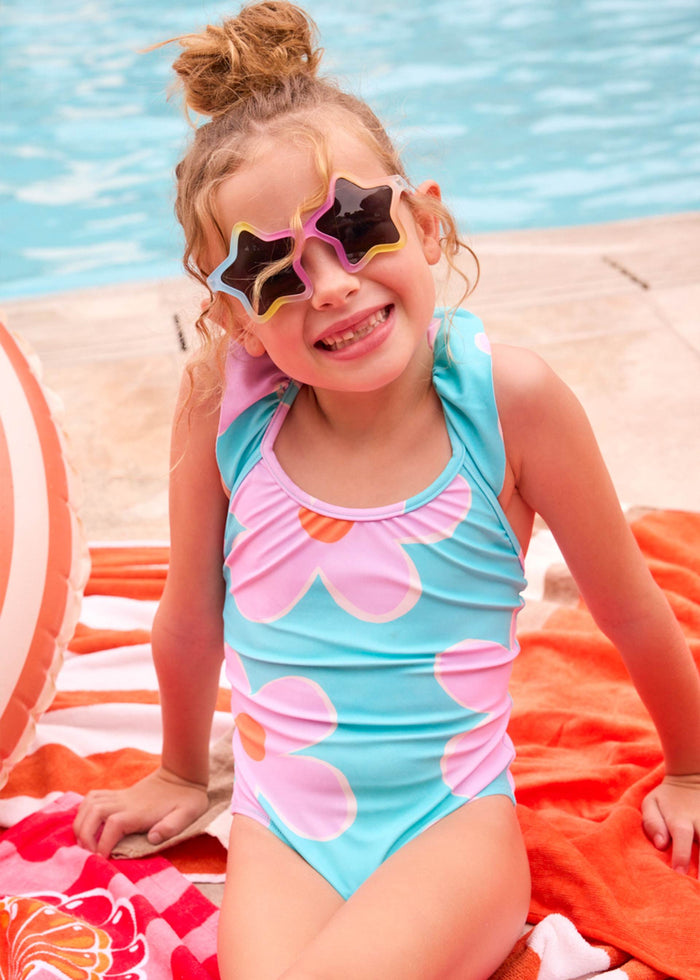 Girl wearing Mayoral ruffled floral swimsuit by the pool on a sunny day