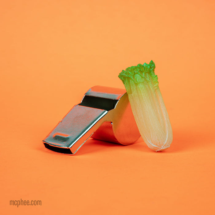 A Glow-in-the-Dark Itty Bitty Celery stalk affixed to a metallic whistle, featured against an orange background.