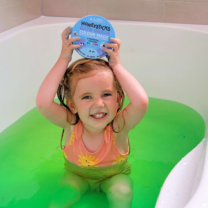 Child in a bathtub holding a tin of Honeysticks bath drops with green water.