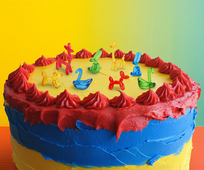A vibrantly frosted cake in red, blue, and yellow is artfully adorned with playful Itty Bitty Balloon Animals.