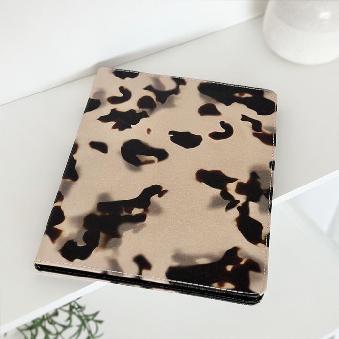 Ivory Tort iPad case with beige and black pattern on a white shelf beside a green plant.