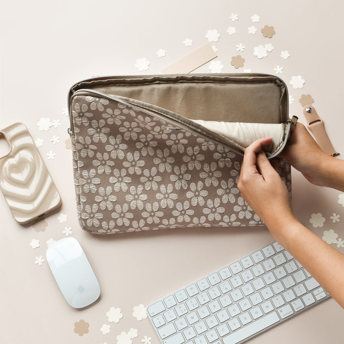 Hands unzipping a brown floral Coconut Lane laptop sleeve on a beige desk with scattered accessories.