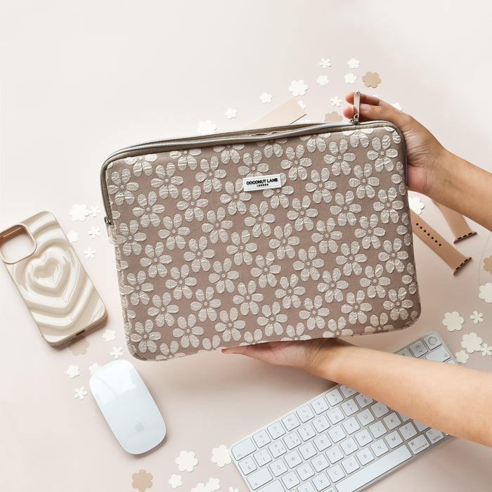Mocha Flower print laptop sleeve held above a white keyboard, mouse, phone, and colorful paper flowers.