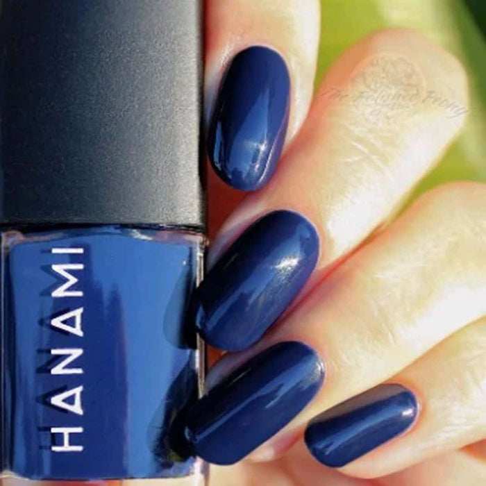 Blue nail polish with a hand displaying nails painted with the same color, next to the Hanami nail polish bottle.